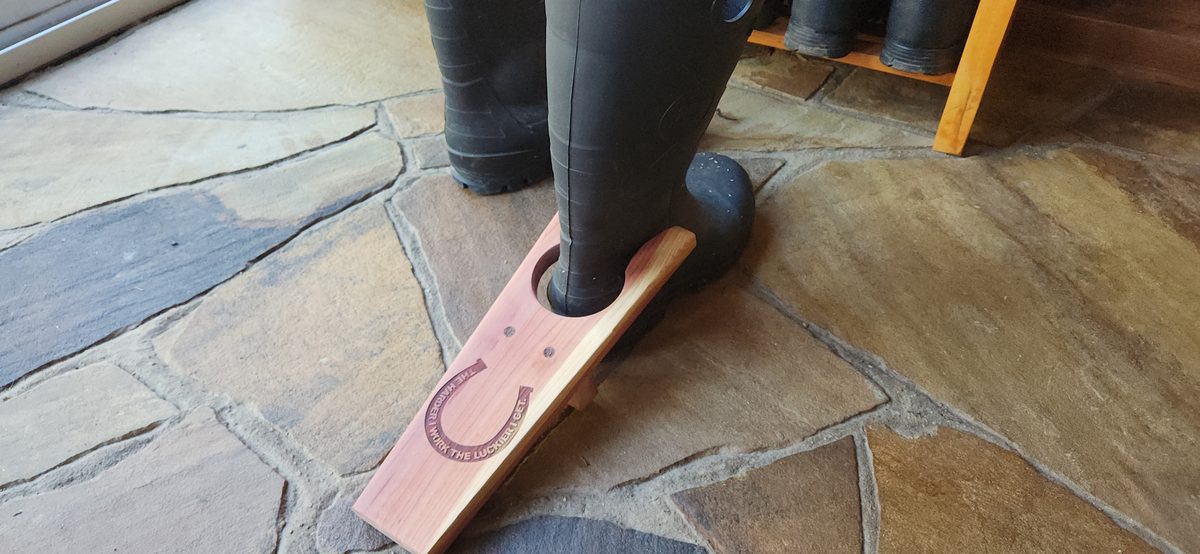 Handmade cedar boot jack with engraved horseshoe, in use with a boot